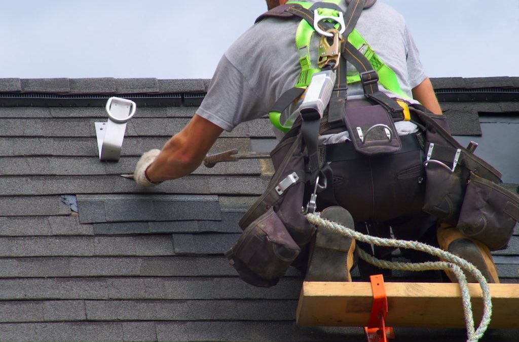 Roofer wearing a safety harness is repairing a roof
